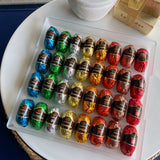 A clear tray of 32 colorful foil-wrapped delights sits atop a white table, next to a classic Leonidas gold ballotin box with a beautiful ribbon - the foils are in a rainbow of colors, each with a label that lists the liqueur within