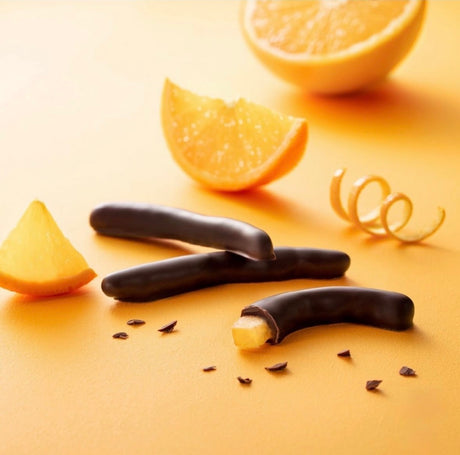 Wedges of orange lay next to three pieces of chocolate-covered candied orange strips