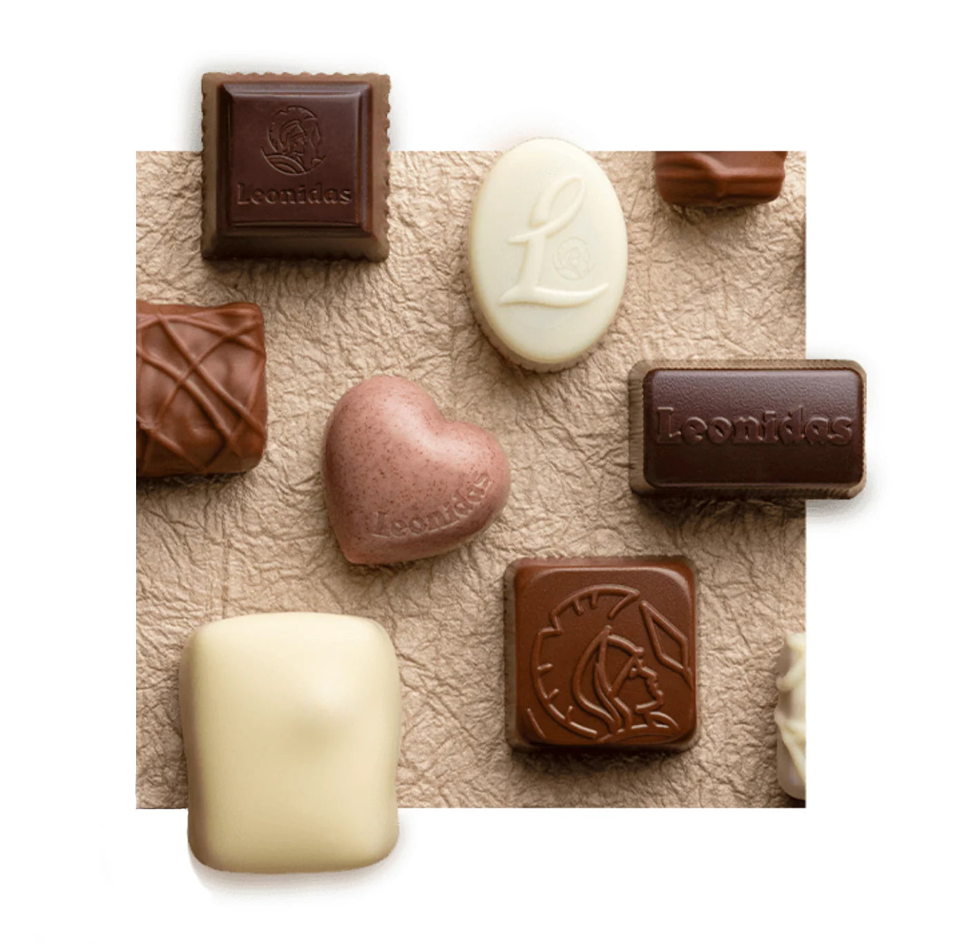 White, milk, and dark chocolates, some imprinted with the Leonidas logo, knolled on a textured piece of beige paper