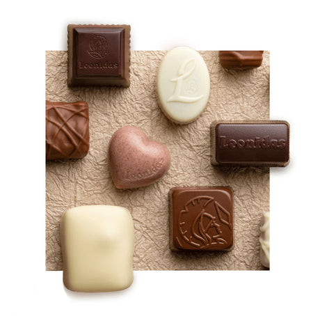 White, milk, and dark chocolates, some imprinted with the Leonidas logo, knolled on a textured piece of beige paper